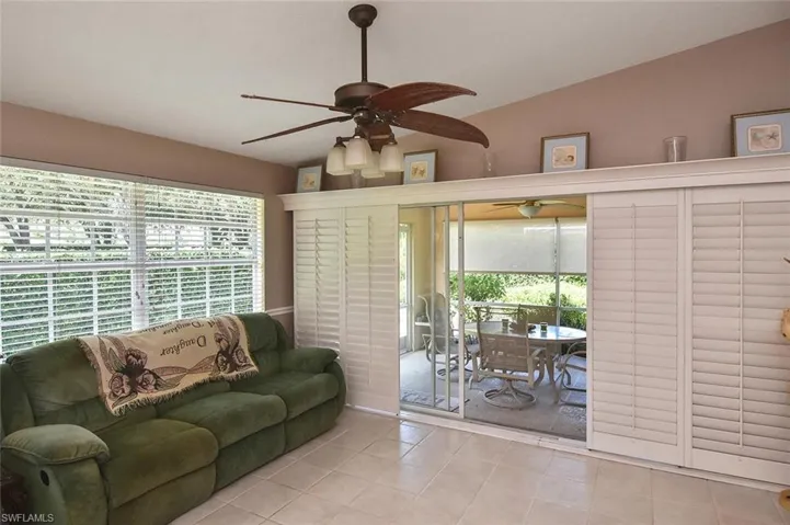Vaulted ceiling with a ceiling fan light fixture, tile flooring, and sliding glass doors with interior shutter panels