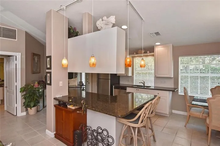 Kitchen featuring a breakfast bar with stone countertop, white cabinetry, and pendant lighting