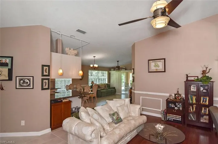 Vaulted ceiling, ceiling fan with integrated lighting, chair rail molding, wall paneling, and an interior pass-through with pendant lighting