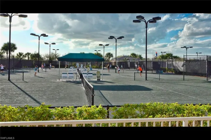 Multiple hard surface tennis courts with permanent nets and surrounding fencing