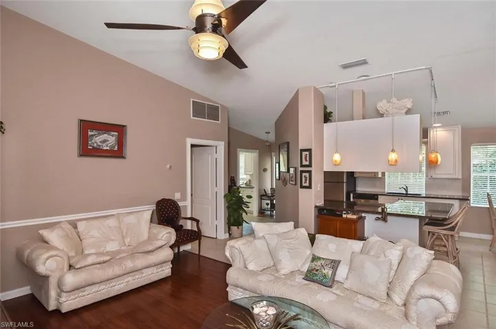 Vaulted ceilings with a ceiling fan, wood-finish flooring, and a kitchen featuring a breakfast bar with pendant lighting and built-in cabinetry