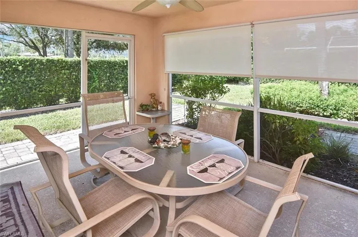 Screened patio featuring a ceiling fan, light-colored walls, roller shades, and a paved outdoor area