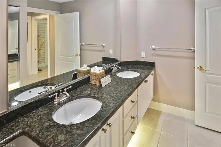 Dual undermount sinks with brushed nickel faucets, dark granite countertop, and white cabinetry