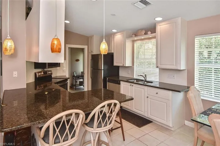 Kitchen featuring a breakfast bar with stone countertops, white cabinetry, stainless steel appliances, and pendant lighting