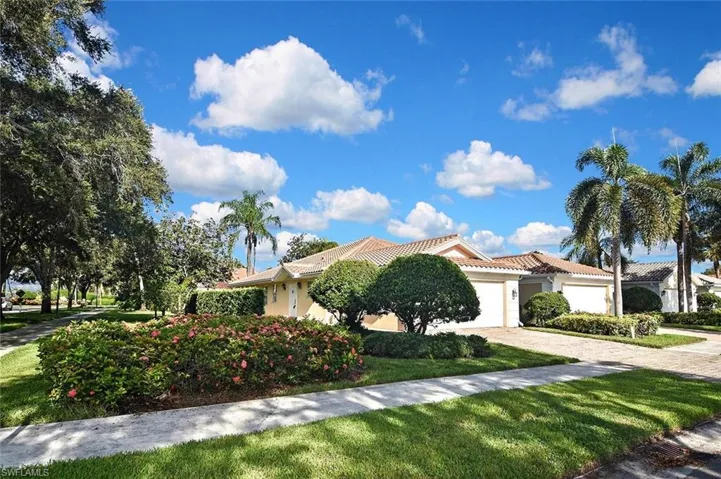 Mediterranean-style residence featuring a tile roof, paved driveway, and mature tropical landscaping