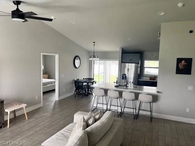 Kitchen featuring hardwood / wood-style floors, a breakfast bar area, vaulted ceiling, ceiling fan with notable chandelier, and stainless steel refrigerator with ice dispenser
