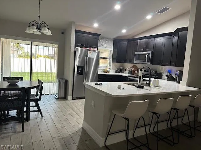 Kitchen featuring hanging light fixtures, light hardwood / wood-style floors, vaulted ceiling, stainless steel appliances, and a notable chandelier