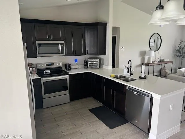 Kitchen featuring kitchen peninsula, appliances with stainless steel finishes, vaulted ceiling, light hardwood / wood-style floors, and sink
