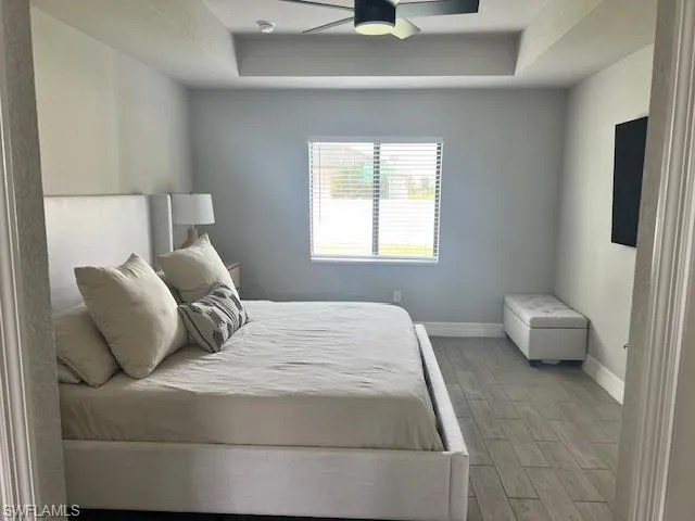 Bedroom featuring light hardwood / wood-style flooring, a raised ceiling, and ceiling fan