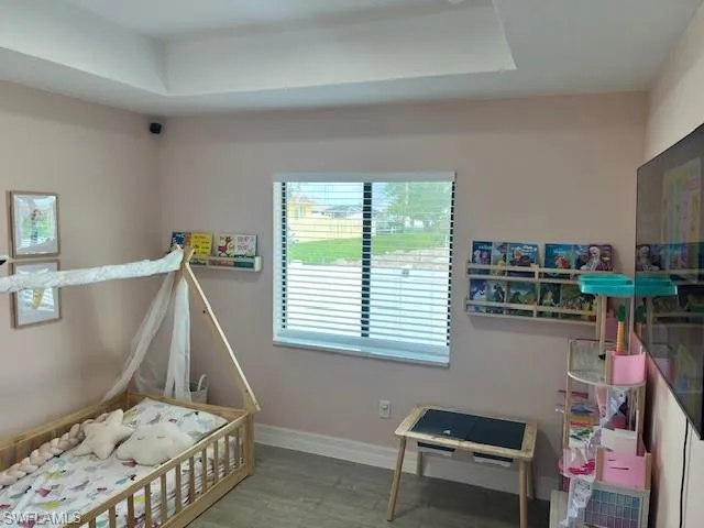 Bedroom with a raised ceiling, wood-type flooring, and a nursery area