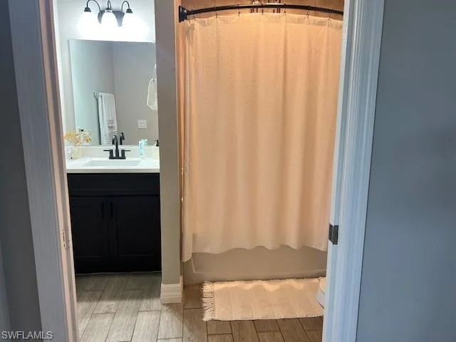 Full bathroom with vanity, hardwood / wood-style flooring, shower / bath combo with shower curtain, and toilet