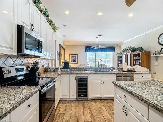 Kitchen with wine cooler, sink, appliances with stainless steel finishes, light wood-type flooring, and crown molding