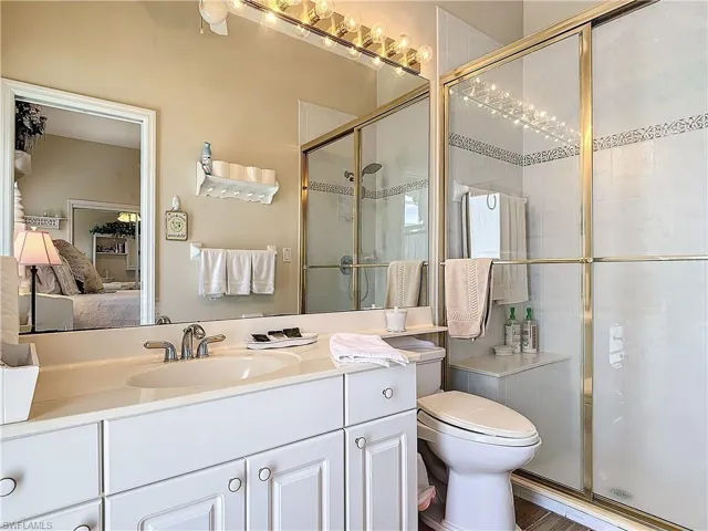 Bathroom featuring wood-type flooring, a shower with shower door, vanity, and toilet