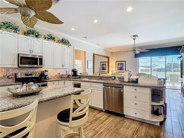 Kitchen featuring ceiling fan, light stone countertops, stainless steel appliances, and white cabinets