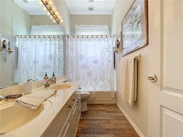 Full bathroom with shower / bath combination with curtain, hardwood / wood-style flooring, vanity, and toilet