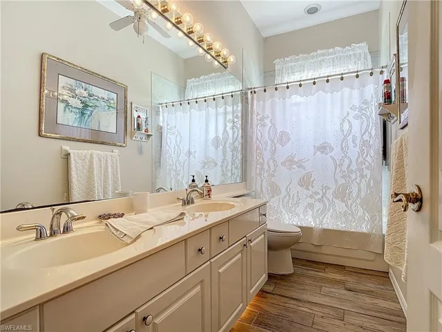 Full bathroom with ceiling fan, shower / bath combination with curtain, vanity, toilet, and hardwood / wood-style floors
