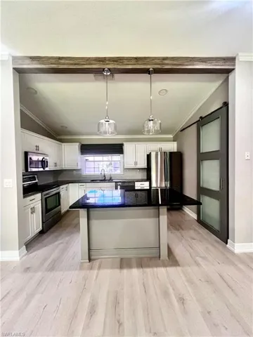 Kitchen featuring appliances with stainless steel finishes, vaulted ceiling, ornamental molding, white cabinetry, and dark countertops