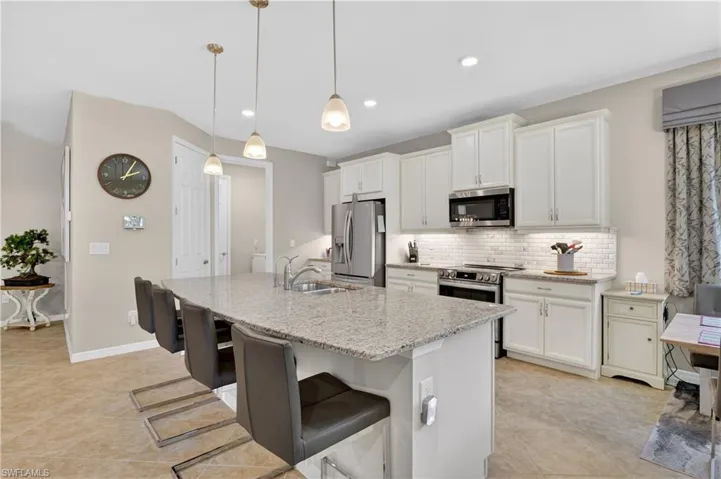 Kitchen with stainless steel appliances, a kitchen island with sink, a kitchen bar, light stone counters, and tasteful backsplash
