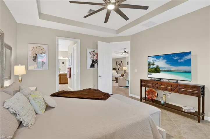 Bedroom with light tile patterned floors, a ceiling fan, a raised ceiling, and connected bathroom