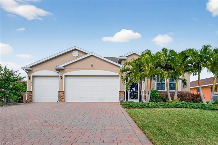 Look at the lush Hibiscus,well manicured yard,featuring stucco siding, a front lawn, stone siding, decorative pavers driveway, and a 3 car garage