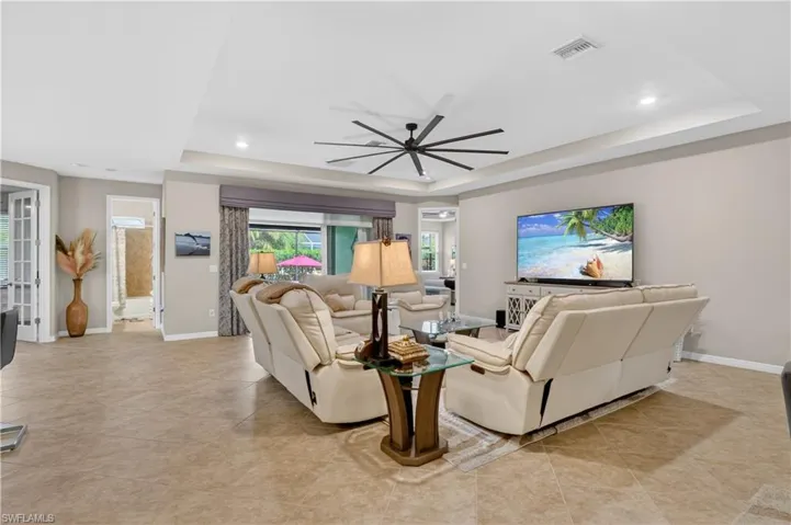 Living room with a raised ceiling, a ceiling fan, recessed lighting, and light tile patterned flooring