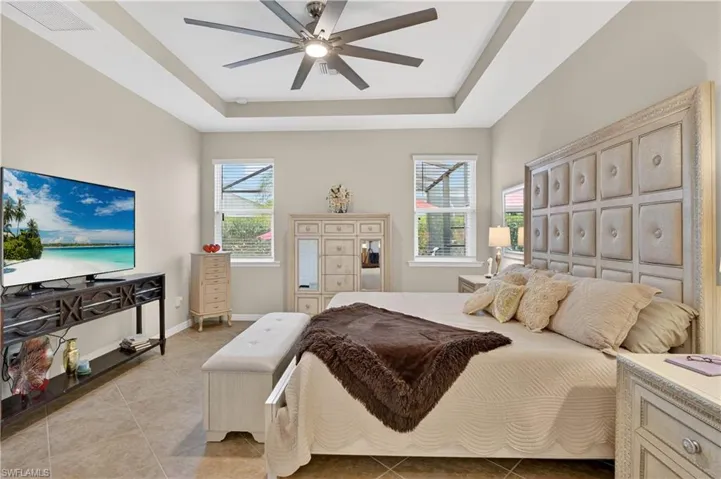 Bedroom with light tile patterned flooring, a raised ceiling, and ceiling fan