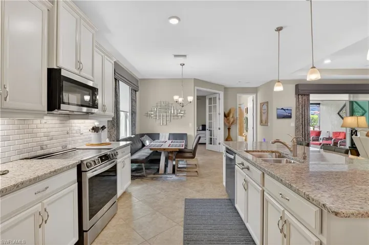 Kitchen with open floor plan, stainless steel appliances, suspended lighting, white cabinets, and light stone counters