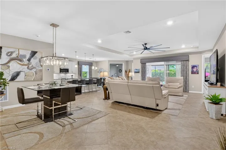 Living area with a tray ceiling, healthy amount of natural light, a ceiling fan, light tile patterned floors, and recessed lighting