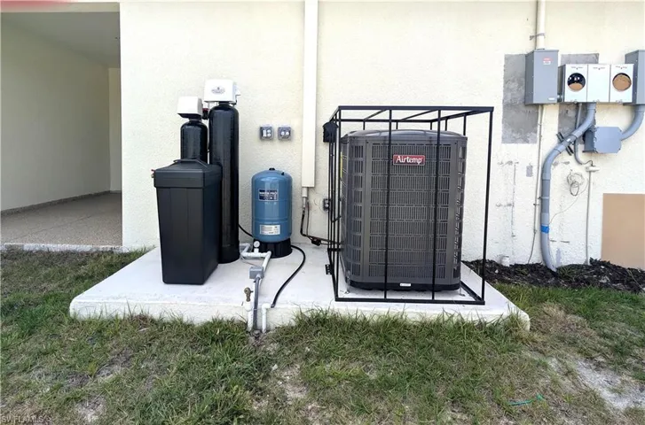 Exterior view of a water softener system, stucco siding, and a water pressure tank