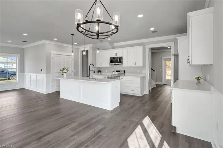 Kitchen featuring white cabinetry, appliances with stainless steel finishes, a center island with sink, and decorative light fixtures