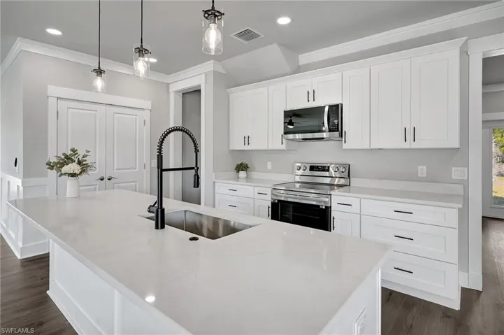 Kitchen with sink, white cabinetry, hanging light fixtures, a center island with sink, and stainless steel appliances