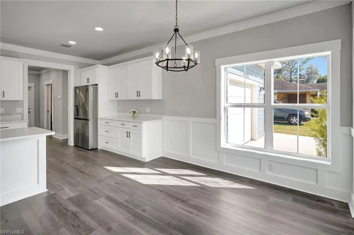 Kitchen featuring white cabinets, ornamental molding, pendant lighting, and stainless steel fridge