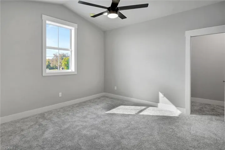 Empty room with lofted ceiling, ceiling fan, and carpet flooring