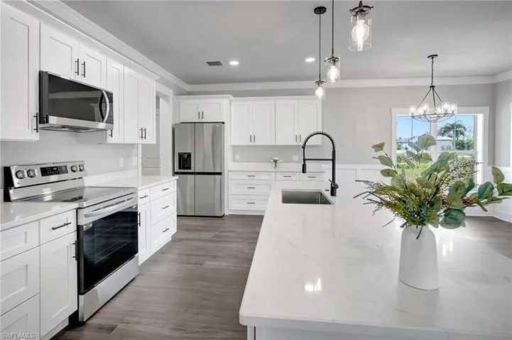 Kitchen with sink, a center island with sink, white cabinets, and appliances with stainless steel finishes