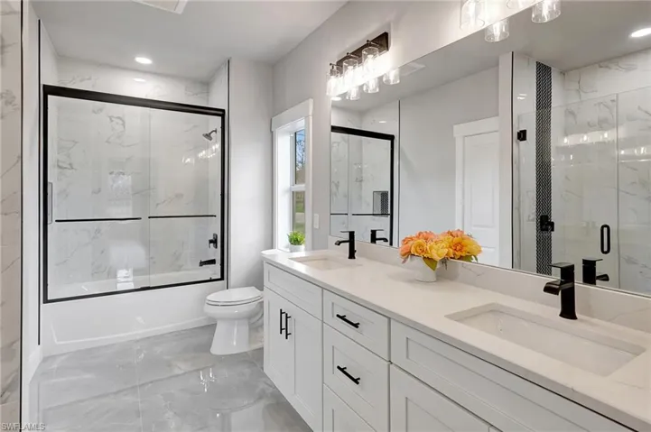 Full bathroom with enclosed tub / shower combo, vanity, and toilet