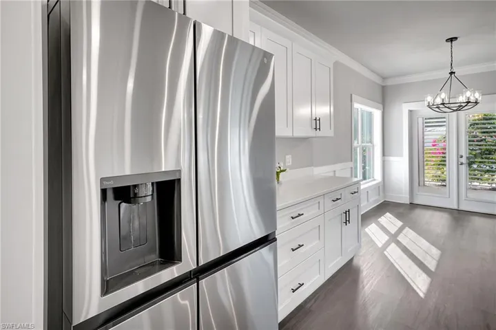 Kitchen with dark wood-type flooring, stainless steel fridge, white cabinetry, hanging light fixtures, and ornamental molding