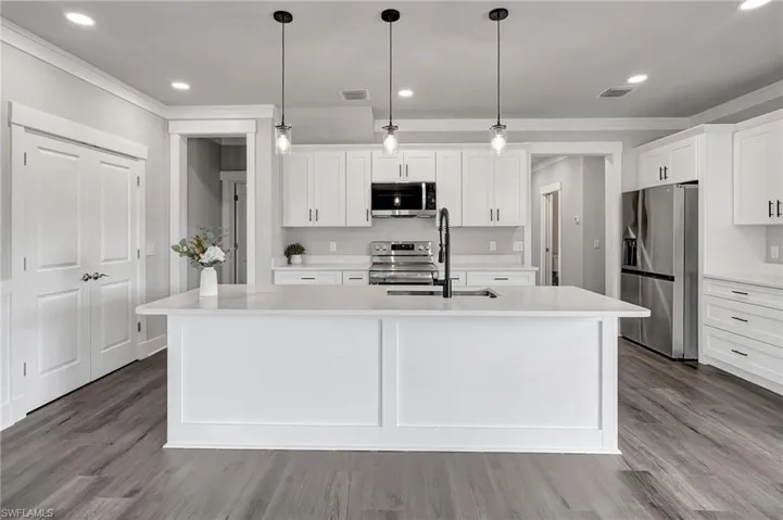 Kitchen featuring sink, stainless steel appliances, white cabinets, a center island with sink, and decorative light fixtures
