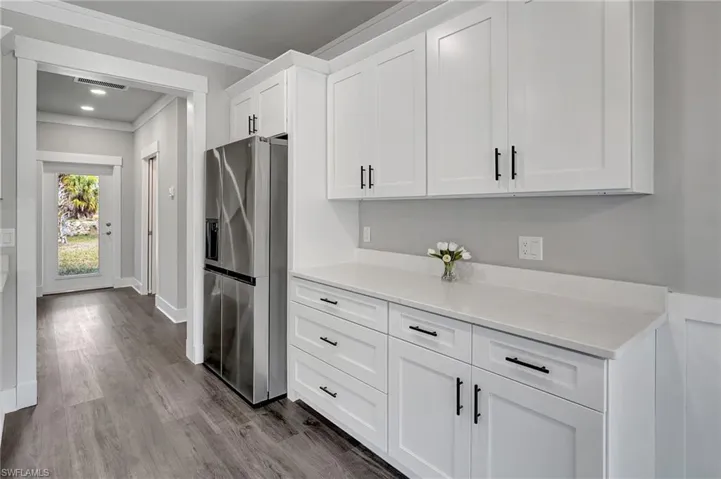 Kitchen with white cabinets, crown molding, light hardwood / wood-style floors, stainless steel refrigerator with ice dispenser, and light stone countertops