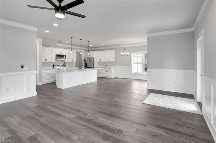 Unfurnished living room with ornamental molding, dark hardwood / wood-style floors, and ceiling fan with notable chandelier