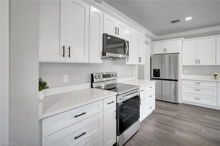 Kitchen with white cabinetry, crown molding, light hardwood / wood-style flooring, and stainless steel appliances