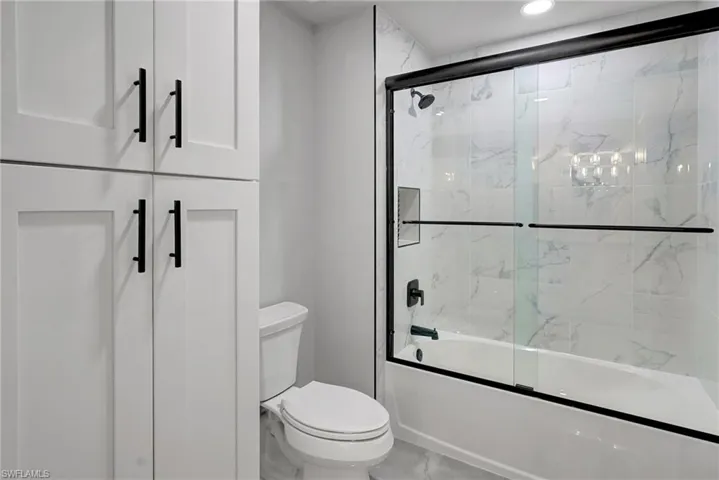 Bathroom with bath / shower combo with glass door and toilet