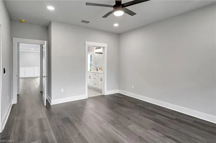 Unfurnished bedroom featuring ensuite bathroom, dark wood-type flooring, and ceiling fan