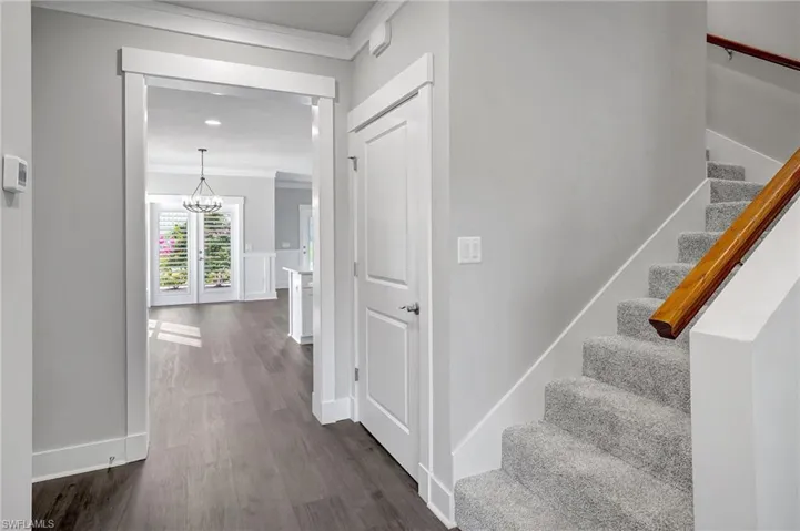 Stairway with a notable chandelier, crown molding, and wood-type flooring
