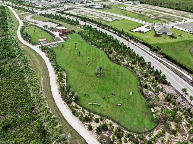 Expansive green space featuring a paved walking path, surrounding natural landscaping, and a dedicated recreational area with structures