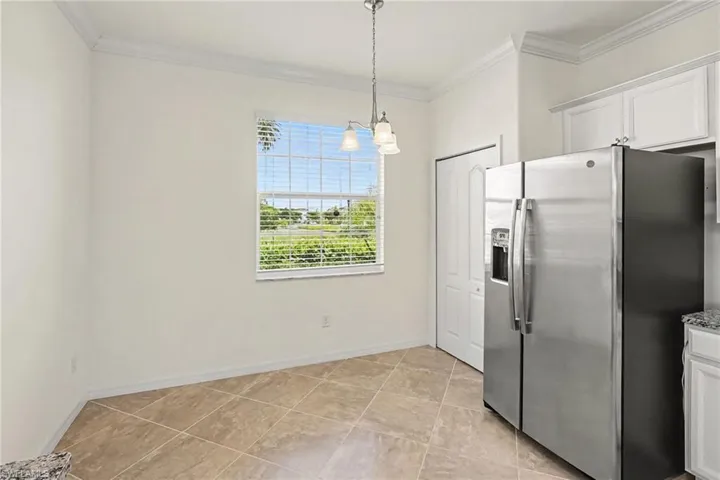 Stainless steel side-by-side refrigerator, white cabinetry, light-toned tile flooring, and a window with horizontal blinds