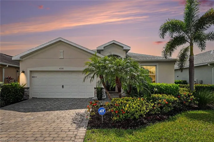 Stucco exterior with a paver driveway, an attached garage, and mature landscaping