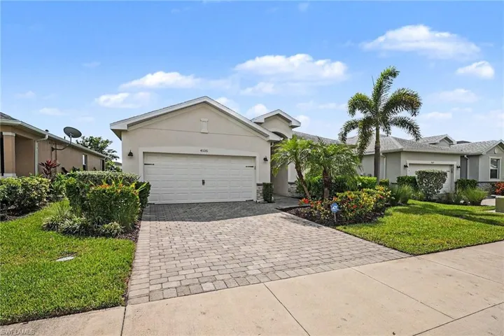 Paver driveway leading to an attached garage, with a stucco exterior and mature landscaping