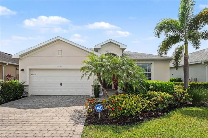 Stucco exterior with stone accents, paver driveway, attached garage, and mature landscaping