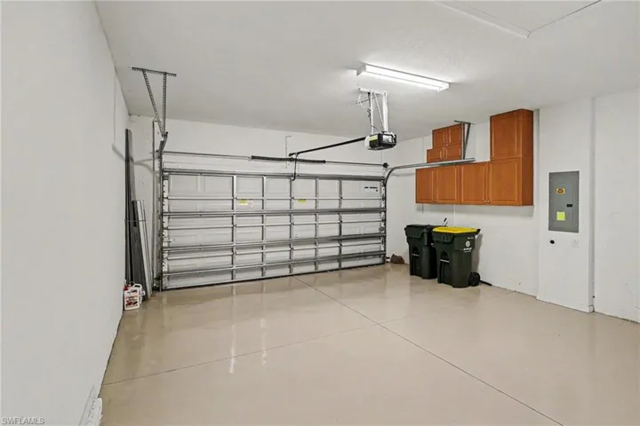 Spacious garage with an automatic overhead door, built-in wooden cabinetry, utility panel, and finished flooring