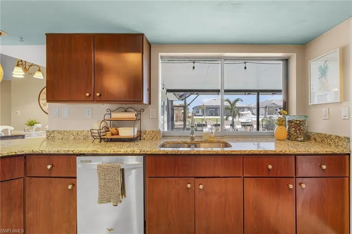 Kitchen with light stone countertops, sink, and stainless steel dishwasher